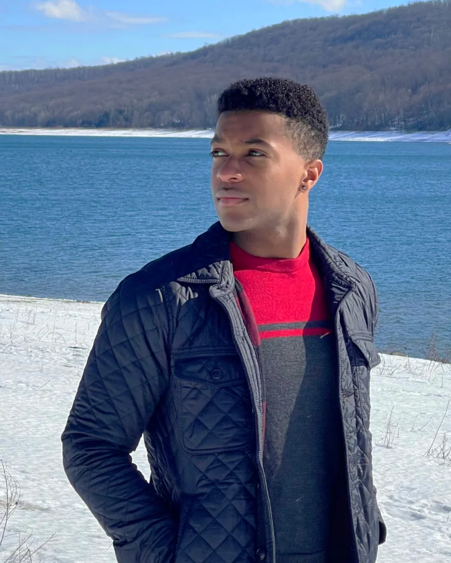 Isaac outdoors beside a wooded reservoir in winter.